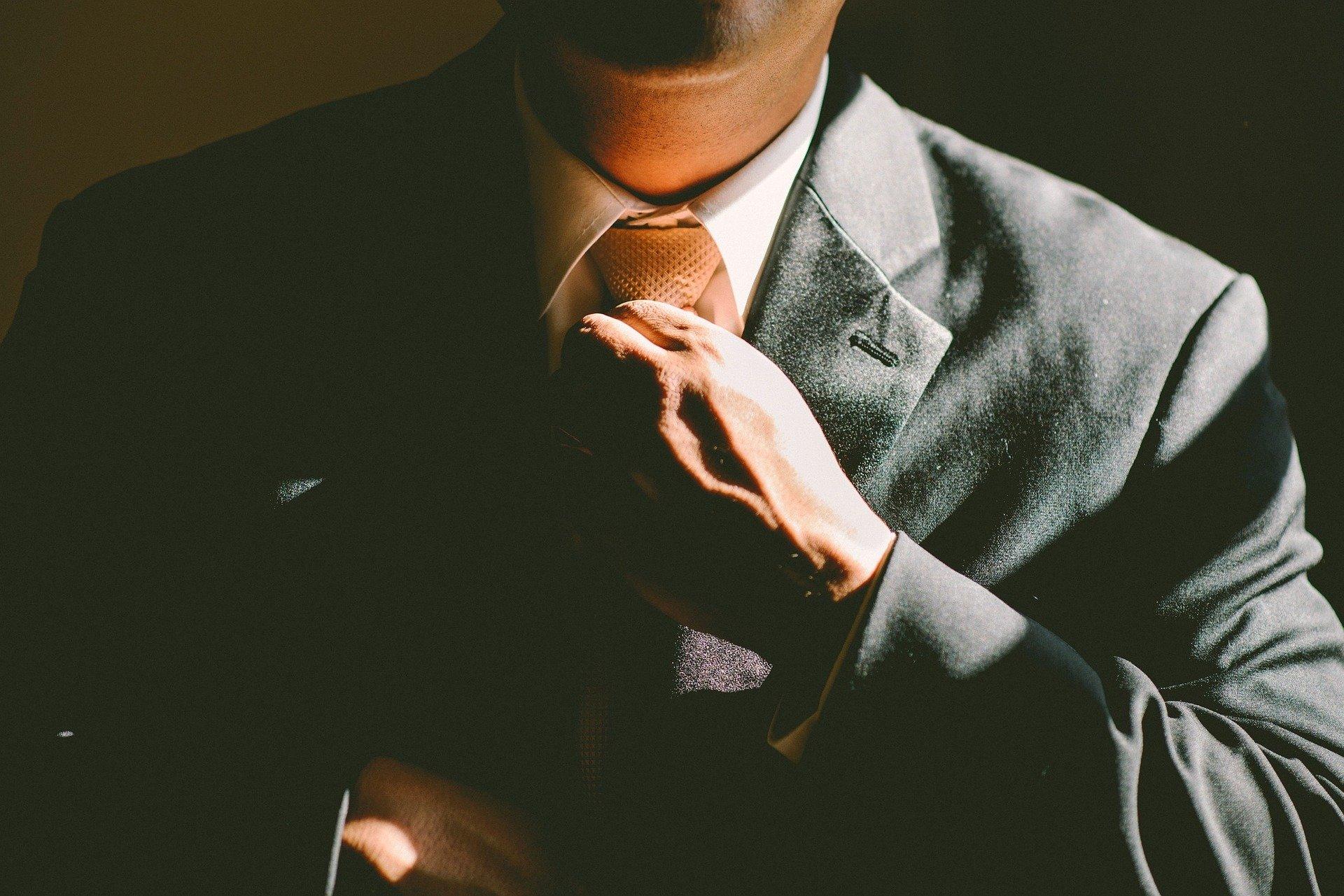 A businessman fixing their tie against a dark background