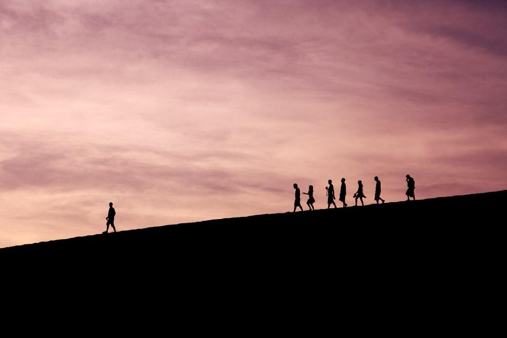 The silhouettes of a leader and his followers going down a hill