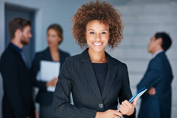 A woman in a suit with her colleagues blurred in the background.